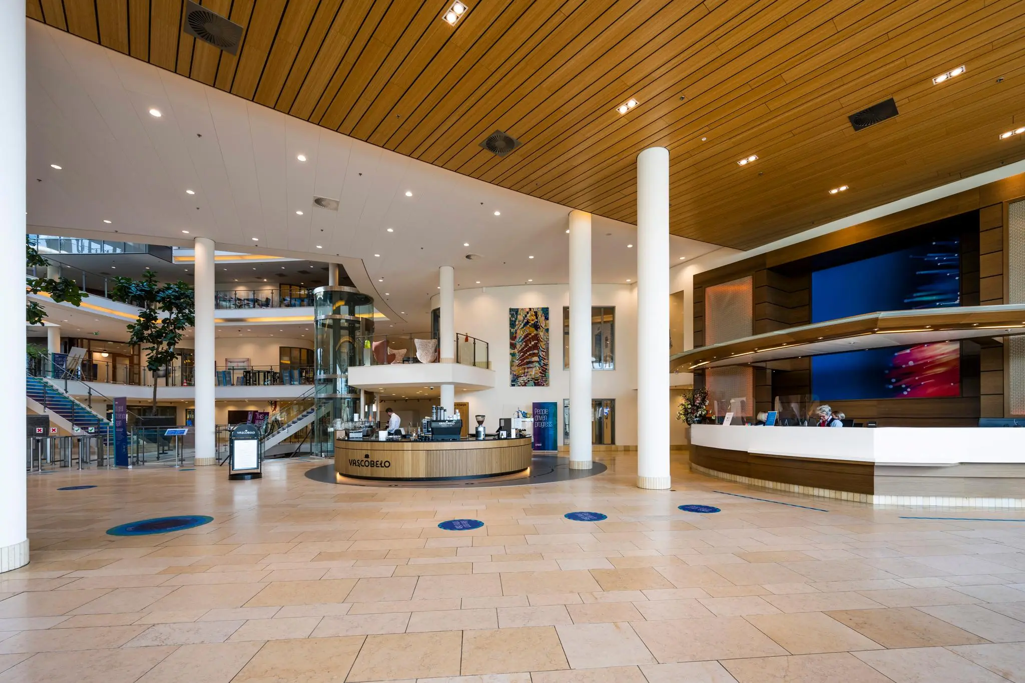 Moderne ontvangsthal van het gebouw aan de Laan van Langerhuize met receptiebalie, koffiebar en glazen lift.